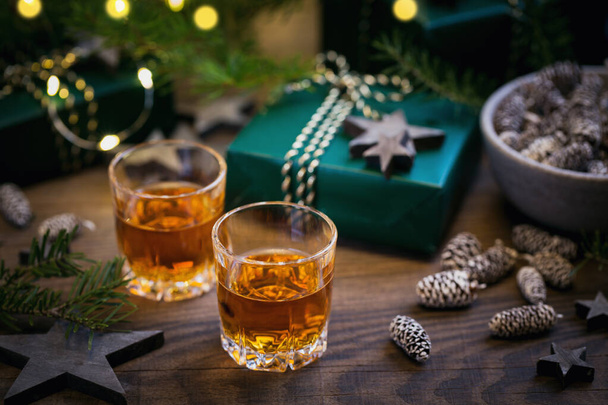 Two glasses of whiskey or bourbon with Christmas decoration on dark background. New Year, Christmas and winter holidays whiskey mood concept - Foto, Imagen