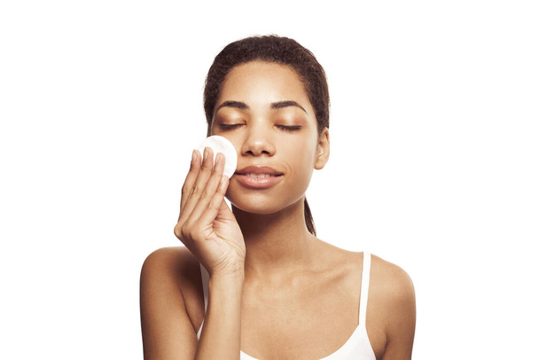 Giovane bella donna afro-americana che pulisce il viso dal trucco con tamponi di cotone bianco su sfondo bianco - Foto, immagini