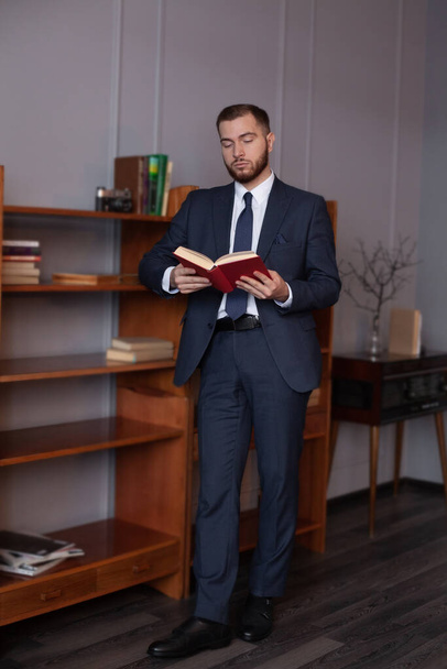 Portrét sebevědomého muže, jak čte knihu, když stojí ve svém obýváku - Fotografie, Obrázek