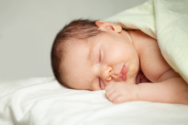 Новорожденный ребенок лежит на кровати на белом фоне - Фото, изображение