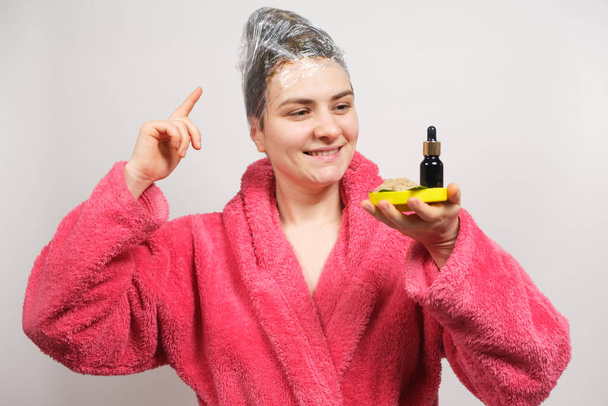 Женщина хранит натуральную косметику для ухода за волосами - бутылку масла и убтана, скраб трав. - Фото, изображение