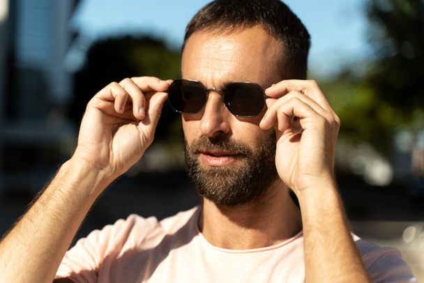Portrait of handsome bearded man wearing stylish sunglasses looking away standing on the street  - Fotó, kép