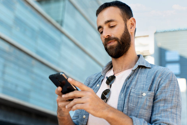Een knappe Spaanse man die online mobiel telefoneert, sms 'jes leest op straat. E-handel   - Foto, afbeelding