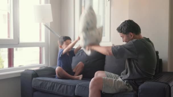 Молодой отец и маленький сын любят драться подушками сидеть дома на диване. Высококачественные 4k кадры - Кадры, видео