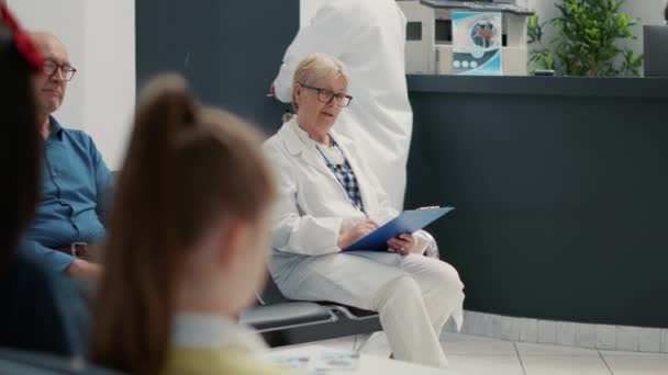 Portrait of senior medical specialist sitting in waiting area lobby at healthcare facility, general practitioner taking notes before doing checkup visit and consultation. Hospital reception desk. - Filmmaterial, Video