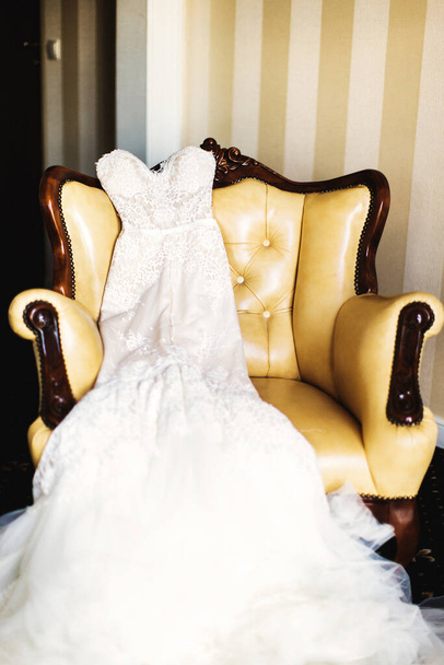 De trouwjurk ligt op een leren fauteuil. - Foto, afbeelding