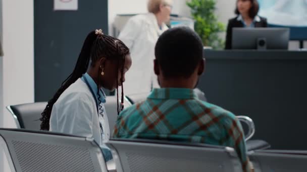 African american physician and patient talking about diagnosis results on medical report files, sitting in hospital waiting area. People doing healthcare consultation in clinic lobby. Close up. - Séquence, vidéo