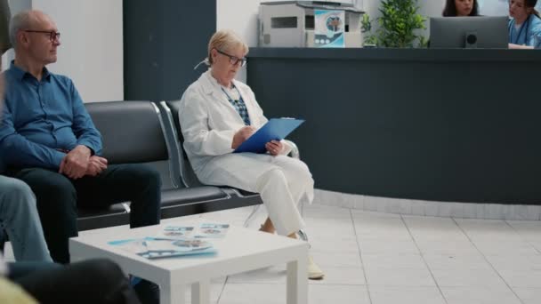 Πορτρέτο της ηλικιωμένης γιατρού που εργάζεται για την έκθεση ελέγχου στην αίθουσα αναμονής στη ρεσεψιόν του νοσοκομείου. Χειρουργός που προετοιμάζεται να συμβουλευτεί ασθενή με νόσο στο ραντεβού εξέτασης. - Πλάνα, βίντεο