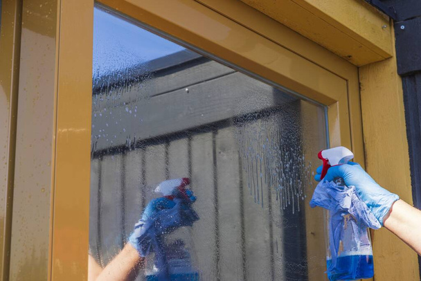 Закройте вид на руку женщины, мойте окна в доме спреем для мытья окон. Швеция. - Фото, изображение
