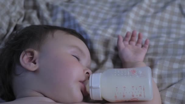 Portrait of a sleeping little child with a bottle in his mouth. The baby eats in a dream. The baby drinks milk from a bottle and sleeps. High quality 4k footage - Video