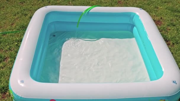 Close up view of children's swimming pool being filled with water from garden hose for swimming on warm summer day. Sweden. - Filmmaterial, Video