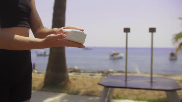 Gymnastics by the sea - a young woman using a talc brick on her hands. Mid shot - Video
