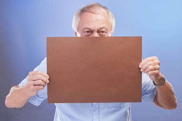 But you didnt hear it from me... Studio shot of a senior man holding a blank sign against a blue background - Photo, image