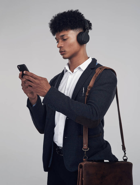 A podcast any professional can relate to. Studio shot of a young businessman using a smartphone and headphones against a grey background - Foto, Imagem