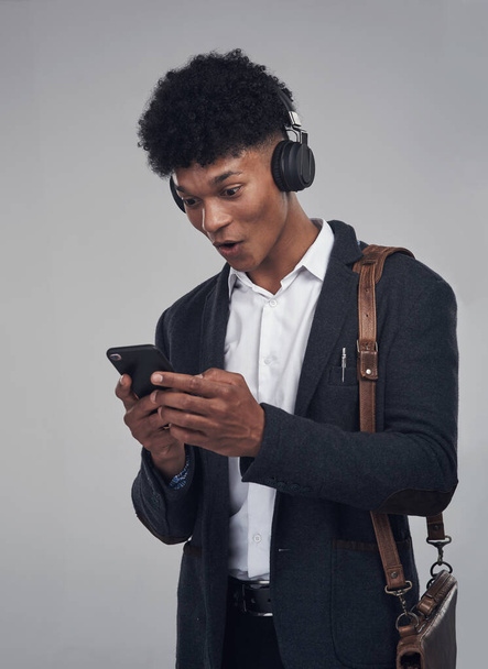 Turn it up and let the music work its magic. Studio shot of a young businessman using a smartphone and headphones against a grey background - Fotó, kép