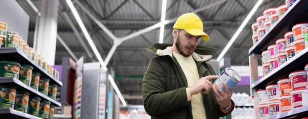 ένας αγοραστής ανάμεσα στα ράφια σε ένα σούπερ μάρκετ με ένα τηλέφωνο στα χέρια του. - Φωτογραφία, εικόνα