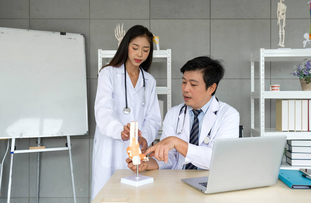 Young asian Orthopedic Surgeons in white gown and stethoscope asking for the professor advice about bone, joint, tendon and muscle. Working atmosphere in hospital. - 写真・画像