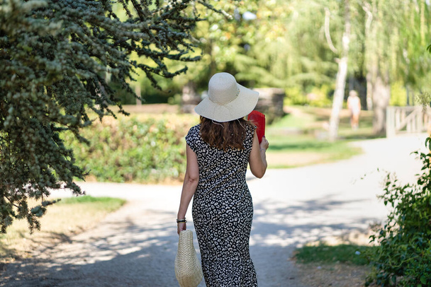 Woman in a hat walking through a public park on a sunny day of mild temperature - 写真・画像