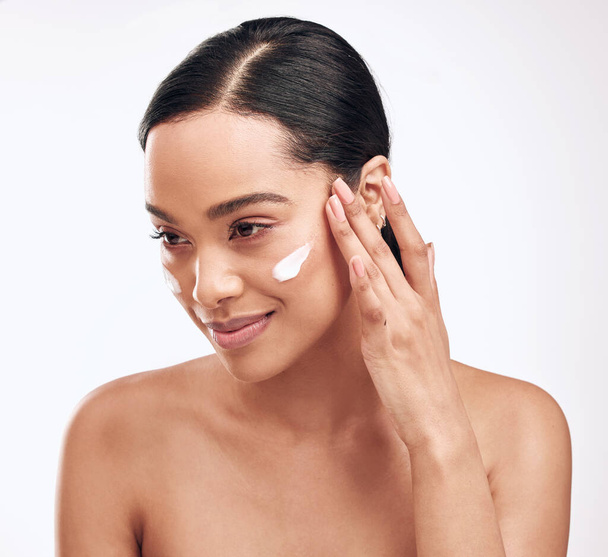 Moisturise to help the youthfulness of your facial skin. Studio shot of a beautiful young woman applying moisturiser to her face - Foto, imagen