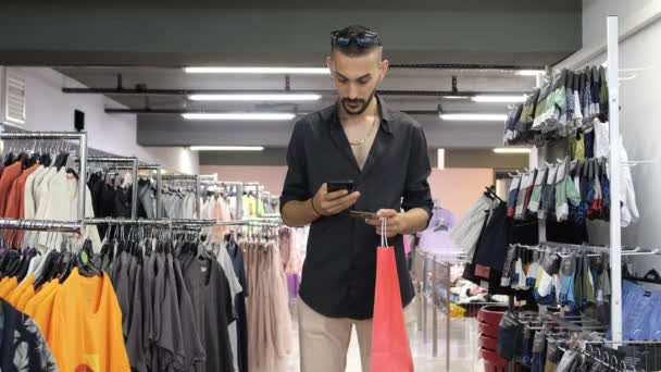 Show your phonescreen in centre, young man show green screen in shopping store, image of shopping from the phone in the clothing aisle - Séquence, vidéo
