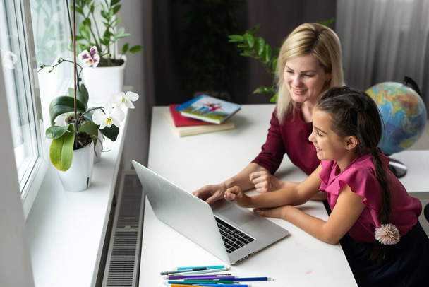 Piękna młoda kobieta i jej córeczka używają laptopa w domu. Cieszymy się razem spędzonym czasem. - Zdjęcie, obraz