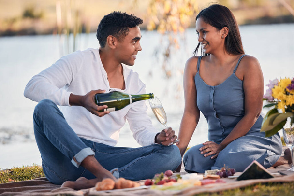 Love is about enjoying the little things in life. a young couple drinking champagne while on a picnic at a lakeside - Foto, afbeelding