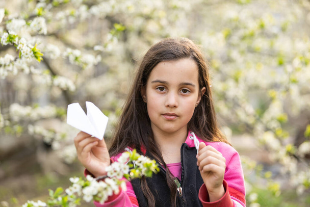 Acima de close-up vista imagem de menina brincando com um avião de papel no parque. Miúdo giro a atirar um avião de papel ao ar livre no jardim. Conceito de infância. - Foto, Imagem