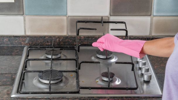 A womans hand in a rubber glove holds the grate from the gas stove to wash the surface - Photo, Image