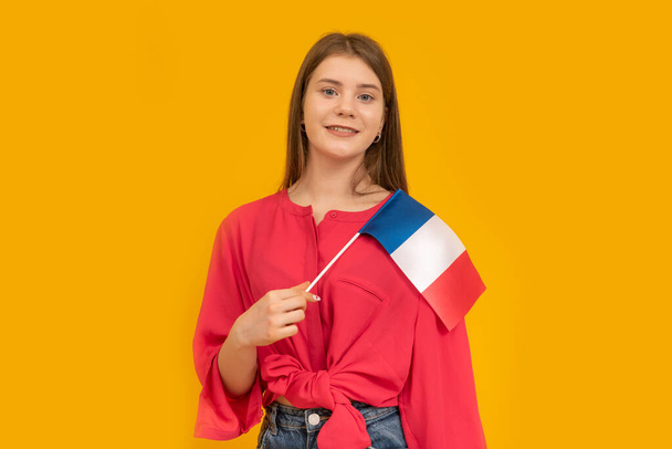 Портрет милої дівчини з прапором Франції в руках на помаранчевому тлі. Вивчи французьку. Імміграція до Франції - Фото, зображення