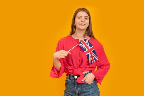 Teenage girl holds the flag of Great Britain on an orange background. Study English. Immigration to the UK - Foto, Imagen