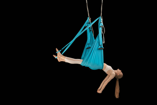 Beautiful young woman is engaged in fly yoga black background. Girl doing antigravity yoga exercises - Fotoğraf, Görsel