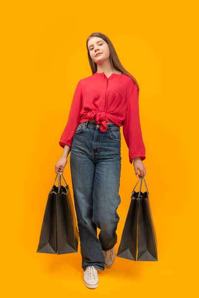 Stylish young girl holds several paper bags after shopping on yellow background. Black Friday Concept. Vertical frame - Foto, Bild