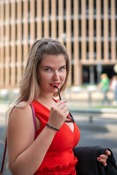 Ellerinde gözlük olan kırmızı elbiseli çekici sarışın kız. Seksi tombul kız portresi - Fotoğraf, Görsel