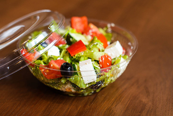 salad with feta cheese, olives and olive oil in plastic box on brown wooden background - Foto, imagen