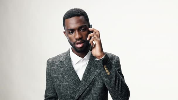 Afro-Amerikaanse man agressief praten aan de telefoon en verdrietig tegen een grijze muur in een kantoor dragen van een business suit en gebaren met zijn handen. Hoge kwaliteit 4k beeldmateriaal - Video