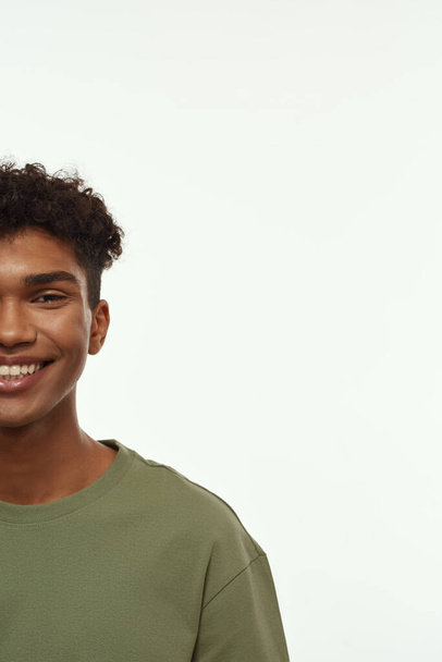 Obscure face of smiling black handsome guy looking at camera. Cropped brunette curly man wearing t-shirt. Concept of modern young male lifestyle. Isolated on white background. Studio shoot. Copy space - Foto, Imagem