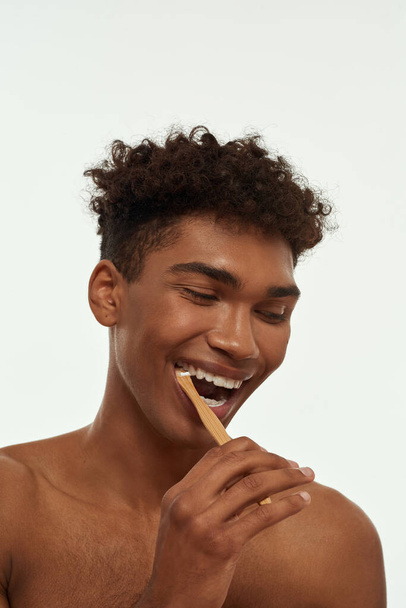 Cropped of excited black guy brushing his teeth with toothpaste. Young positive brunette curly man with naked torso. Dental care and hygiene. Isolated on white background. Studio shoot - Foto, immagini
