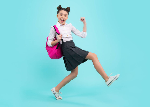 Amazed teenager. School girl in school uniform with backpack. Teenage girl student on blue isolated background. Learning knowledge and kids education concept. Jump and run. Excited teen girl - Fotó, kép