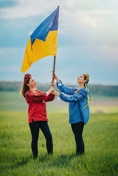 Happy ukrainian women raised national flag, it flies as symbol of love for Motherland. Friends in embroidery vyshyvanka - national blouses. Ukraine, independence, patriot symbol. High quality photo - 写真・画像