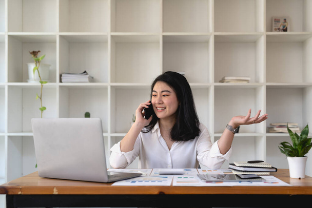 Young asian woman talking on mobile phone in office. Smiling businesswoman making a phone call - Foto, afbeelding