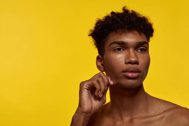 Cropped image of thoughtful black handsome guy looking away. Young brunette curly model man. Concept of modern male beauty. Isolated on yellow background. Studio shoot. Copy space - Фото, зображення