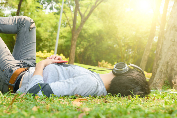 young man resting in the grass with eyes closed listening to music on headphones - Foto, Bild