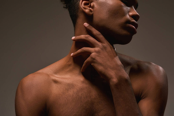 Partial image of african american handsome guy posing on brown background. Obscure face of young brunette man with naked torso. Concept of modern male beauty. Studio shoot - Fotó, kép