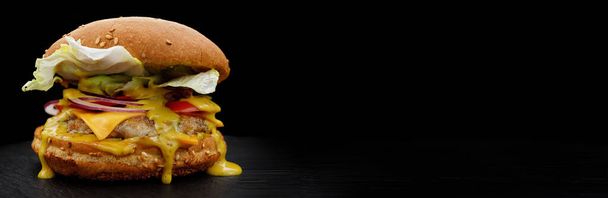 Hamburger zblízka s hovězím masem, rajčaty, salátem, sýrem a cibulí na černém pozadí. Rychlé občerstvení s místem pro váš text. selektivní zaměření - Fotografie, Obrázek