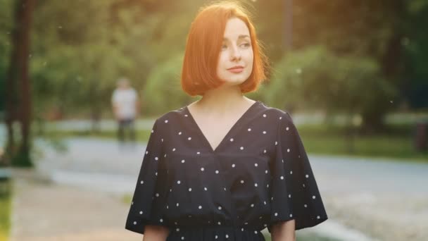 Young redhead sensuality woman attractive female model girlfriend lady wears summer light dress standing alone in city park thoughtful looking for boyfriend resting lonely spend vacation time outdoors - Materiał filmowy, wideo