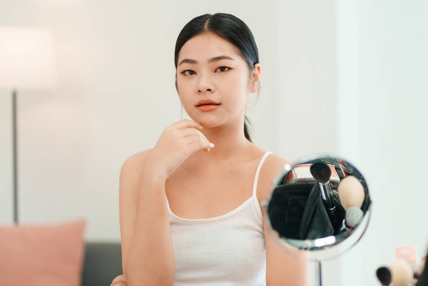 Closeup portrait of smiling young beautiful asian woman looking at mirror touching her skin enjoying treatment for dry skin.  - Zdjęcie, obraz