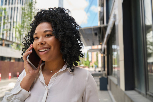 Cute smiling multiracial lady talking on the phone on the streets of a modern city - Foto, imagen