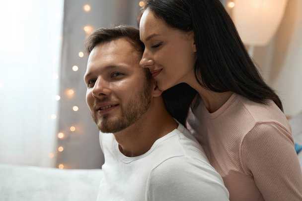 Young man and woman participate in a romantic photo shoot in a cozy bedroom decorated with a garland - Foto, afbeelding