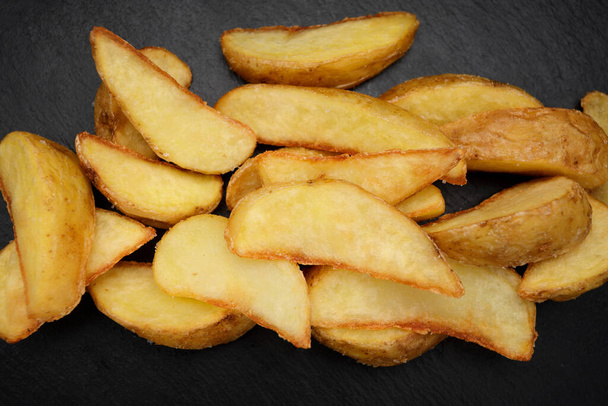 Fried potato wedges on black round slate, dark concrete with nothing - 写真・画像