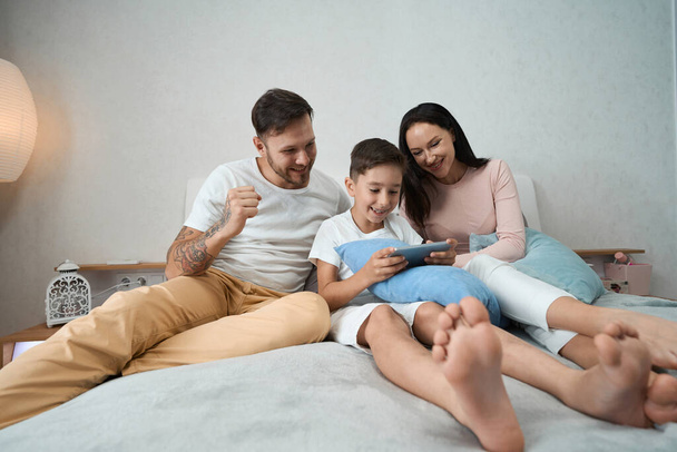 Joyful dad, mom and child spend time together looking at wonderful family photos on the phone - Photo, image
